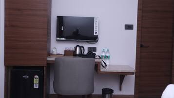 Habitación de hotel con cama, escritorio, monitor de computadora, silla, cafetera y refrigerador.
