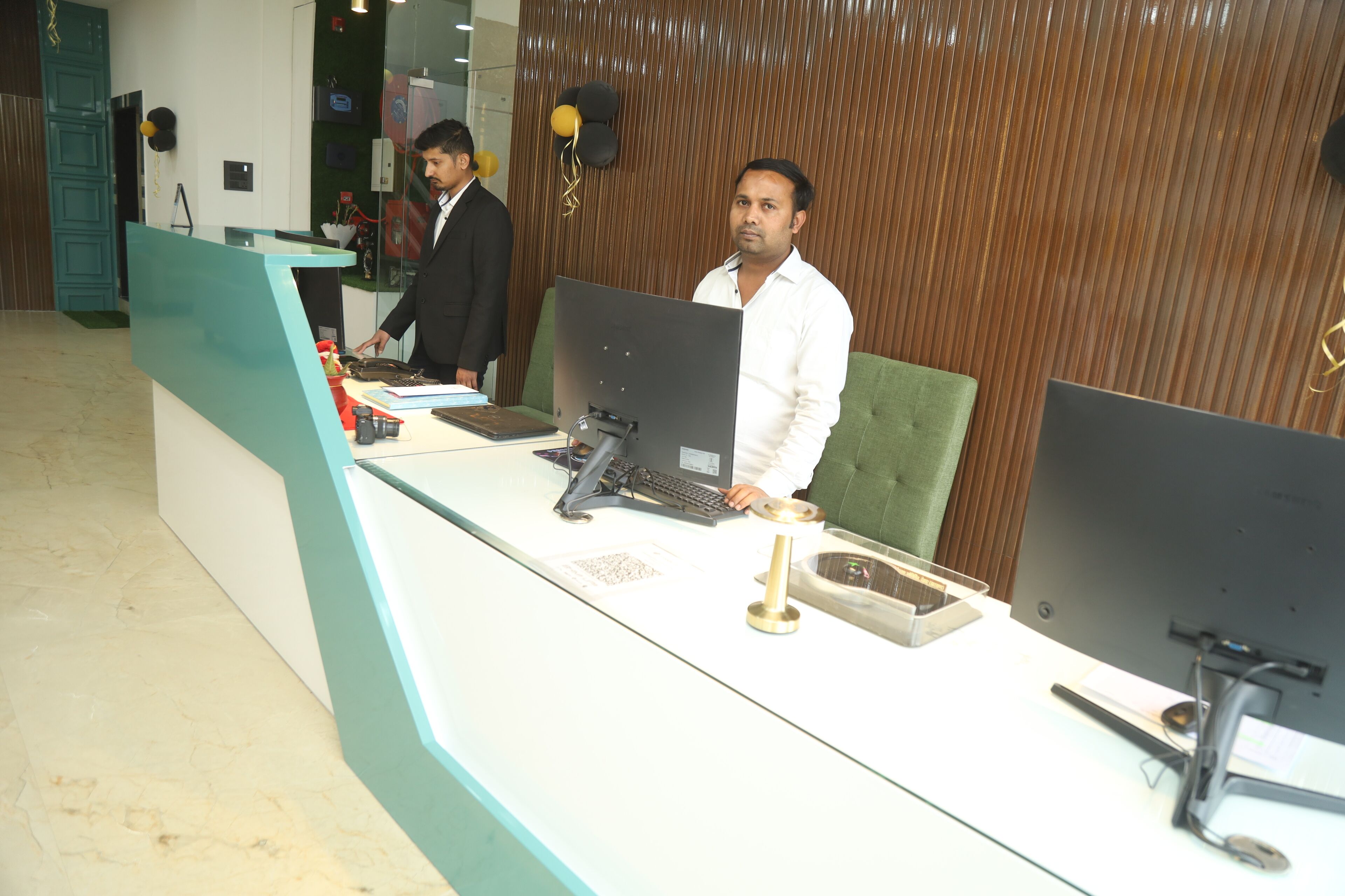 A reception desk with two computer monitors, a keyboard, and a telephone. There is a green cushioned chair behind the desk.