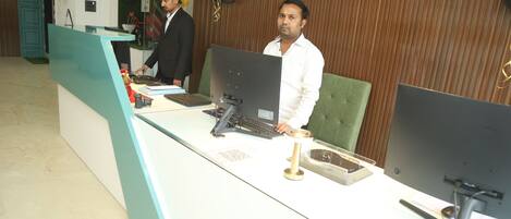 A reception desk with two computer monitors, a keyboard, and a telephone. There is a green cushioned chair behind the desk.
