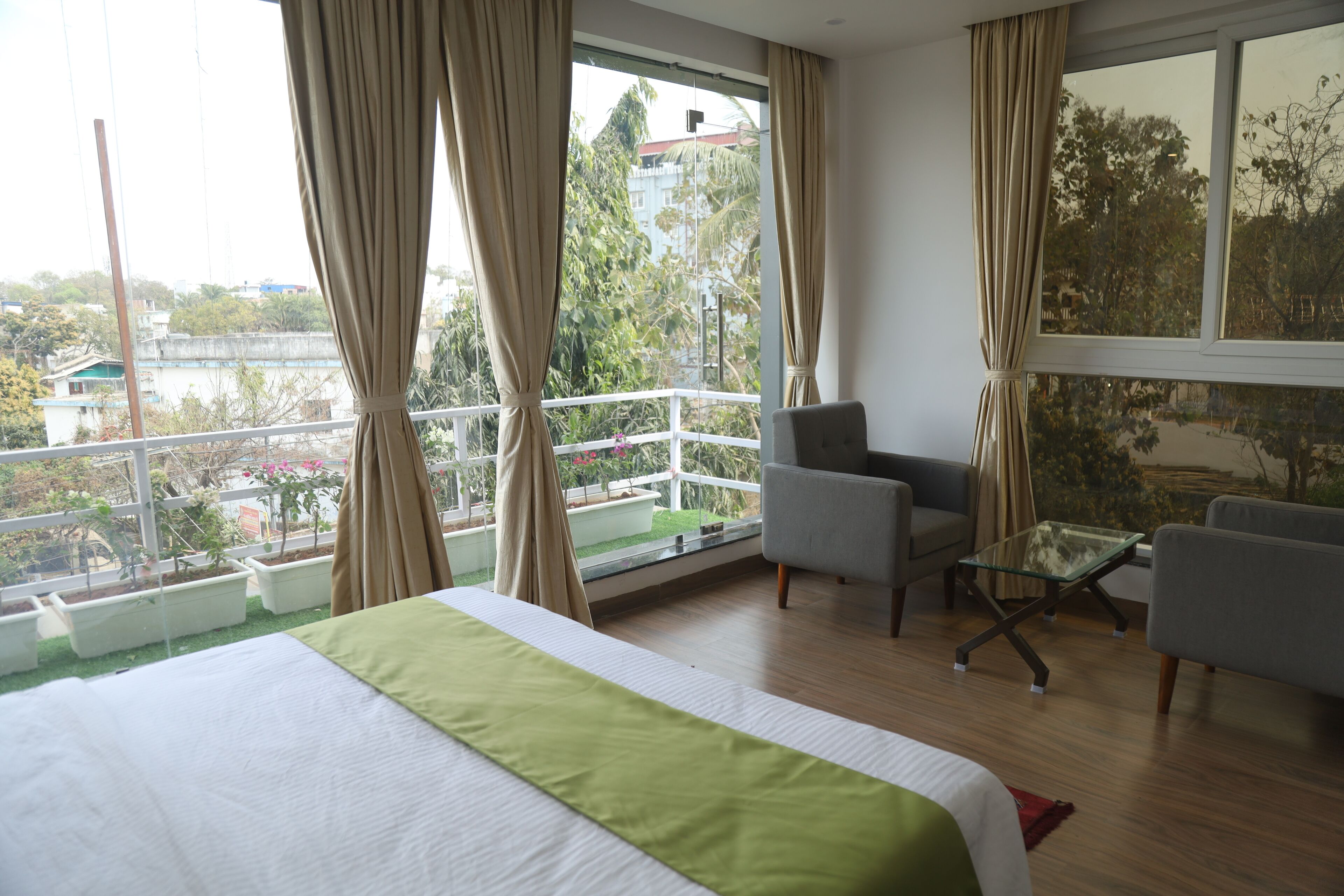 A hotel room with a bed, a sofa, a glass coffee table, and a balcony with potted plants.