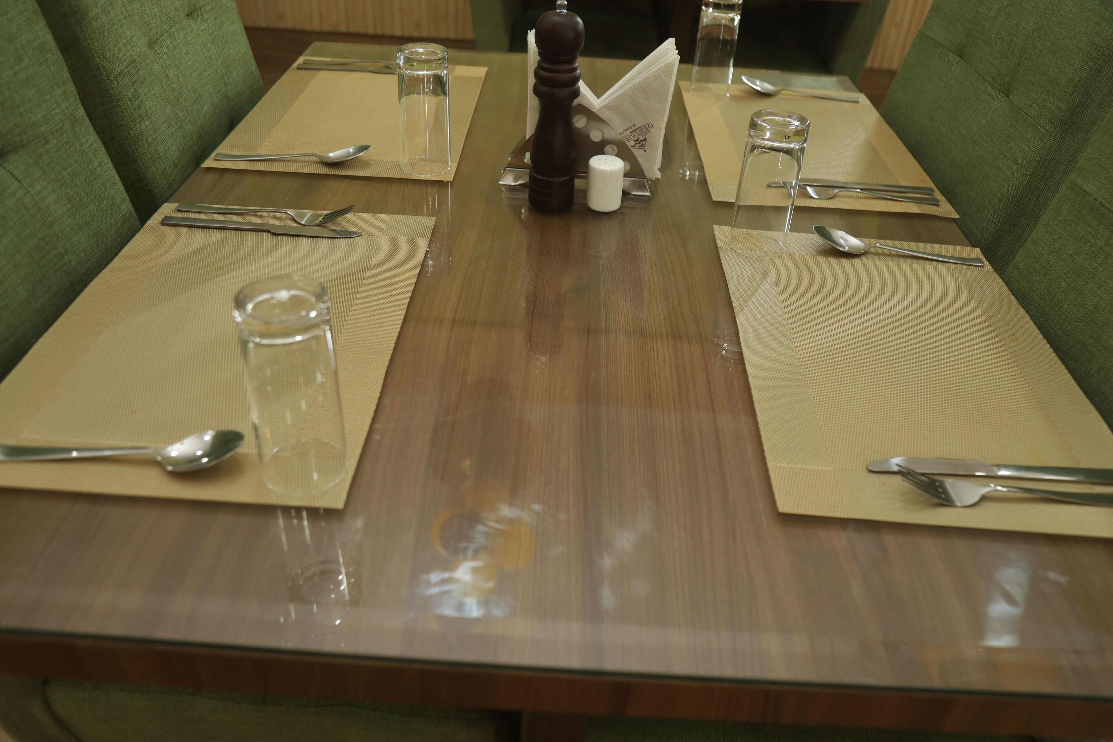 Una mesa de comedor dispuesta con cubiertos y vasos, rodeada de sillas tapizadas en tono verde.