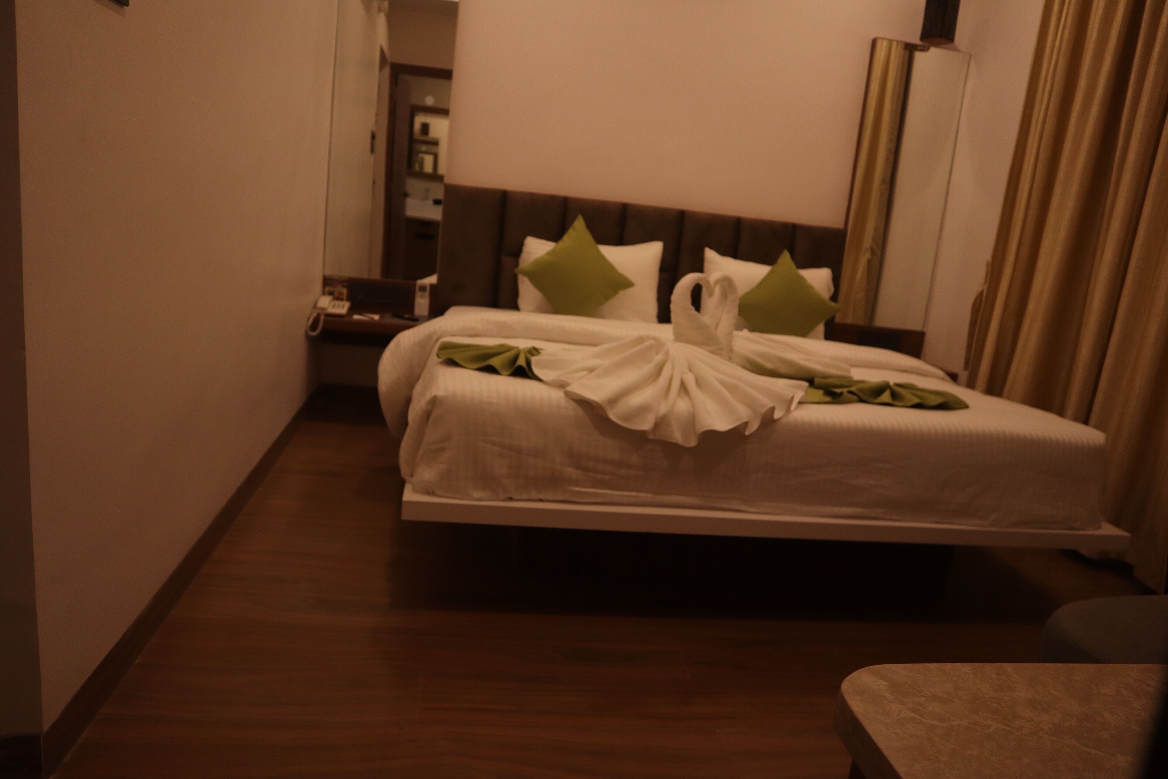 A hotel room with a large bed, a bedside table, and a mirror.