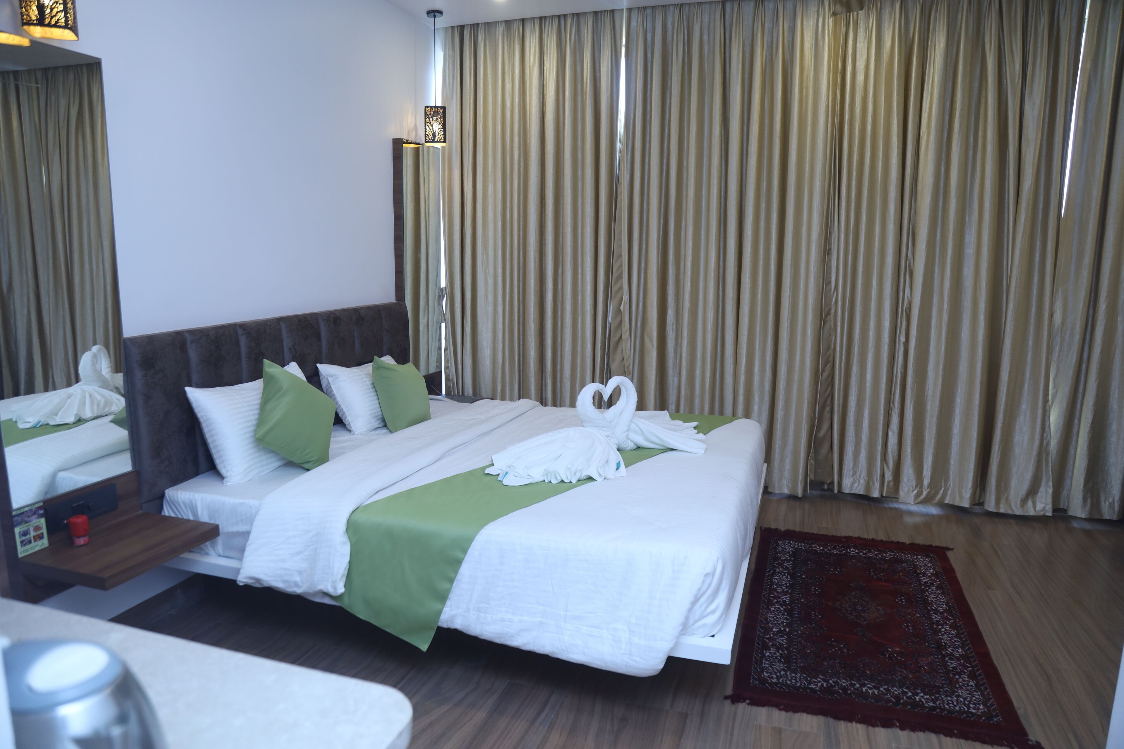 Quarto de hotel com uma cama grande, mesa de cabeceira, espelho, janela com cortinas e um tapete vermelho.