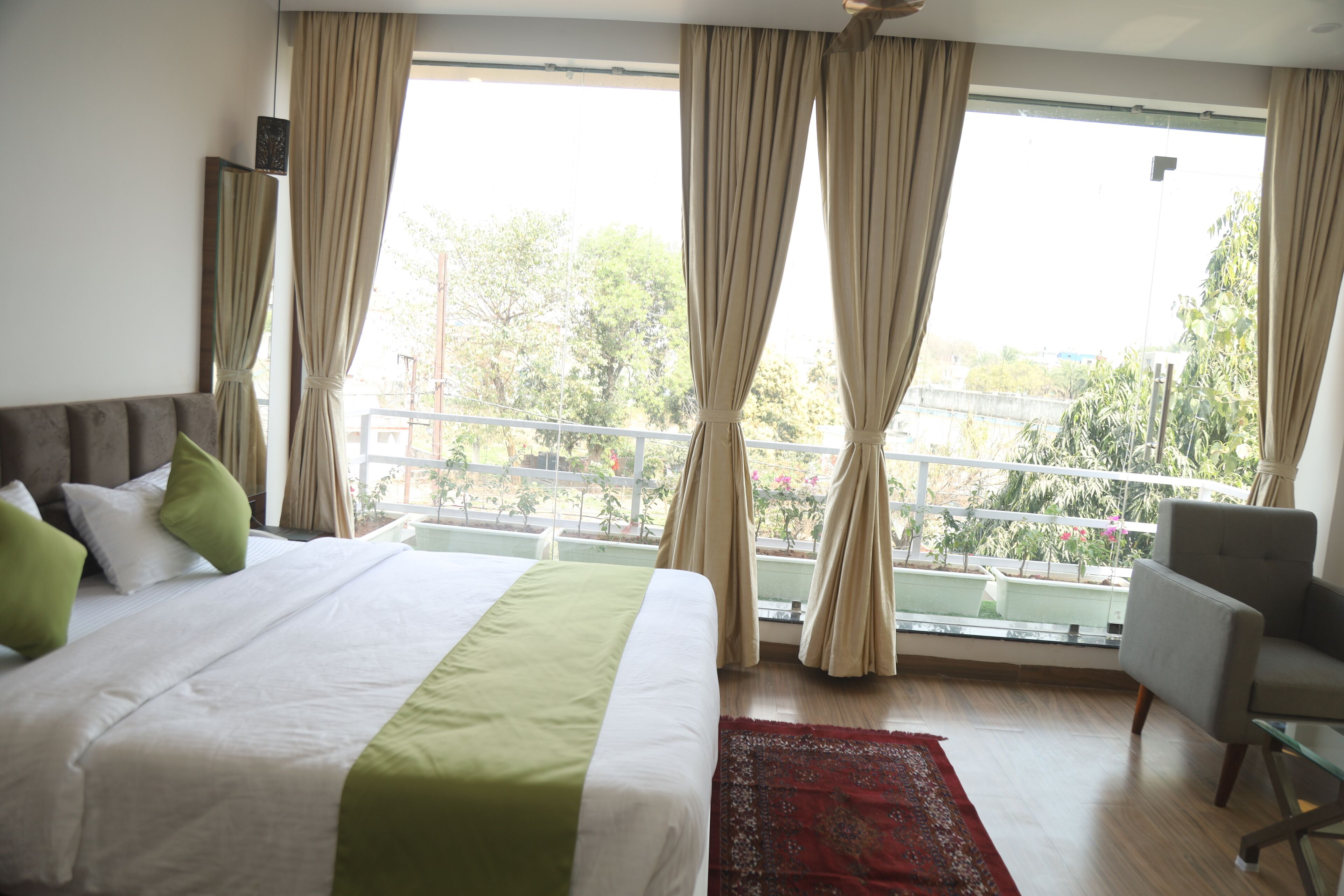 A hotel room with a large bed, a chair, a balcony with a railing, and curtains.