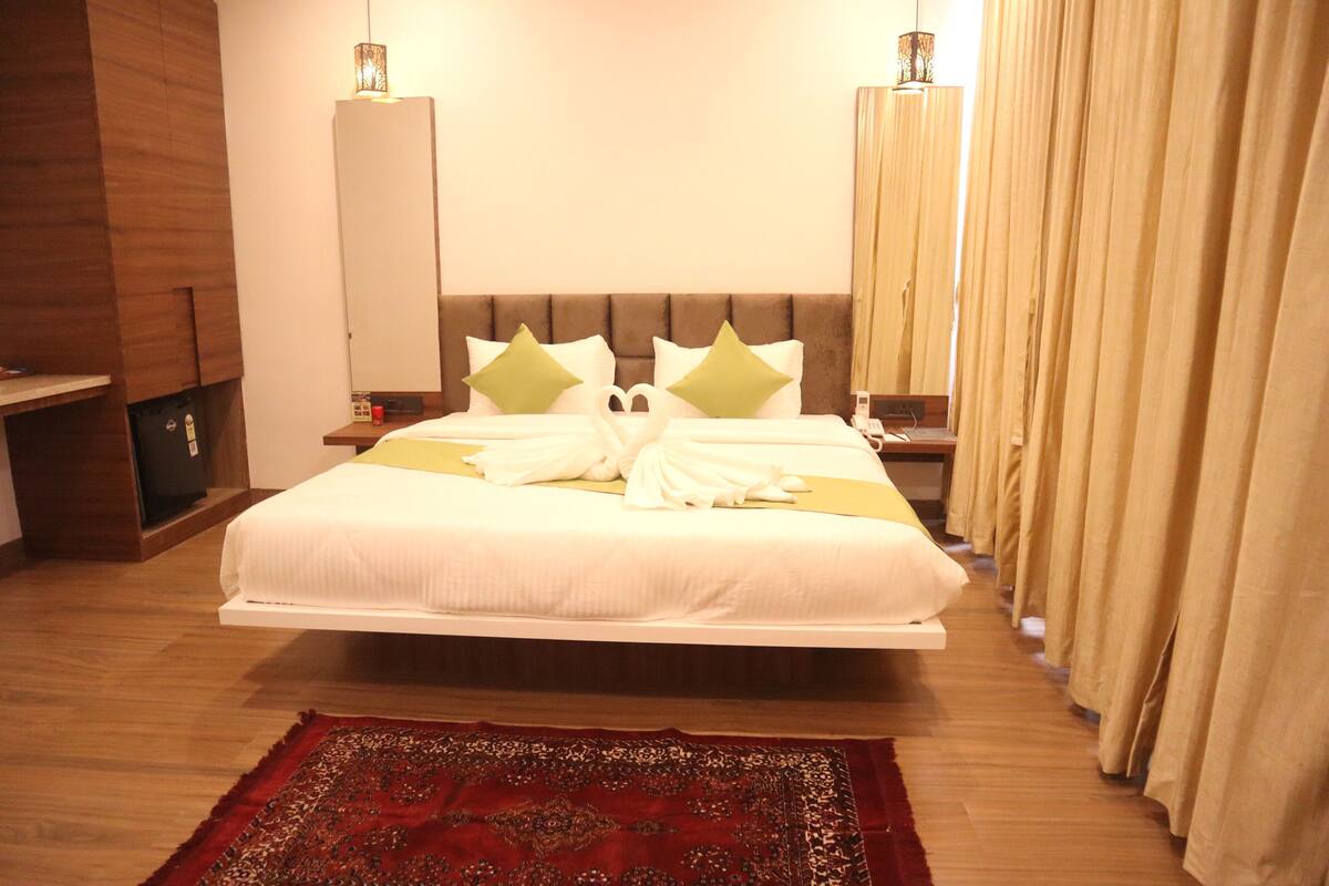 A spacious bedroom with a large bed, a wooden headboard, a bedside table, and a red patterned rug.