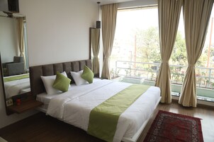Habitación de hotel con una cama grande, una mesita de noche, un espejo y vistas al exterior.