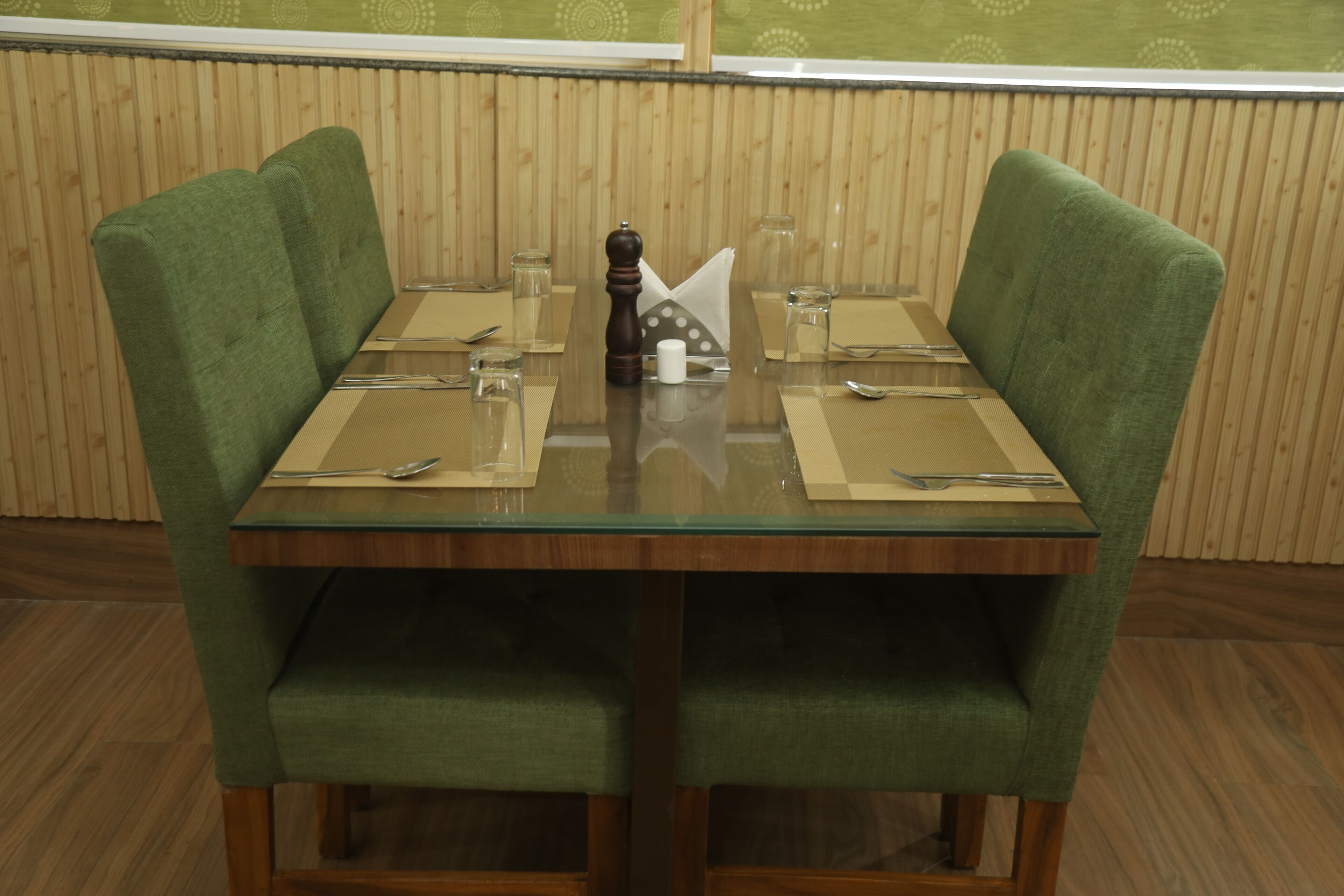 A dining table with green upholstered chairs, a wooden floor, and a wooden paneled wall.