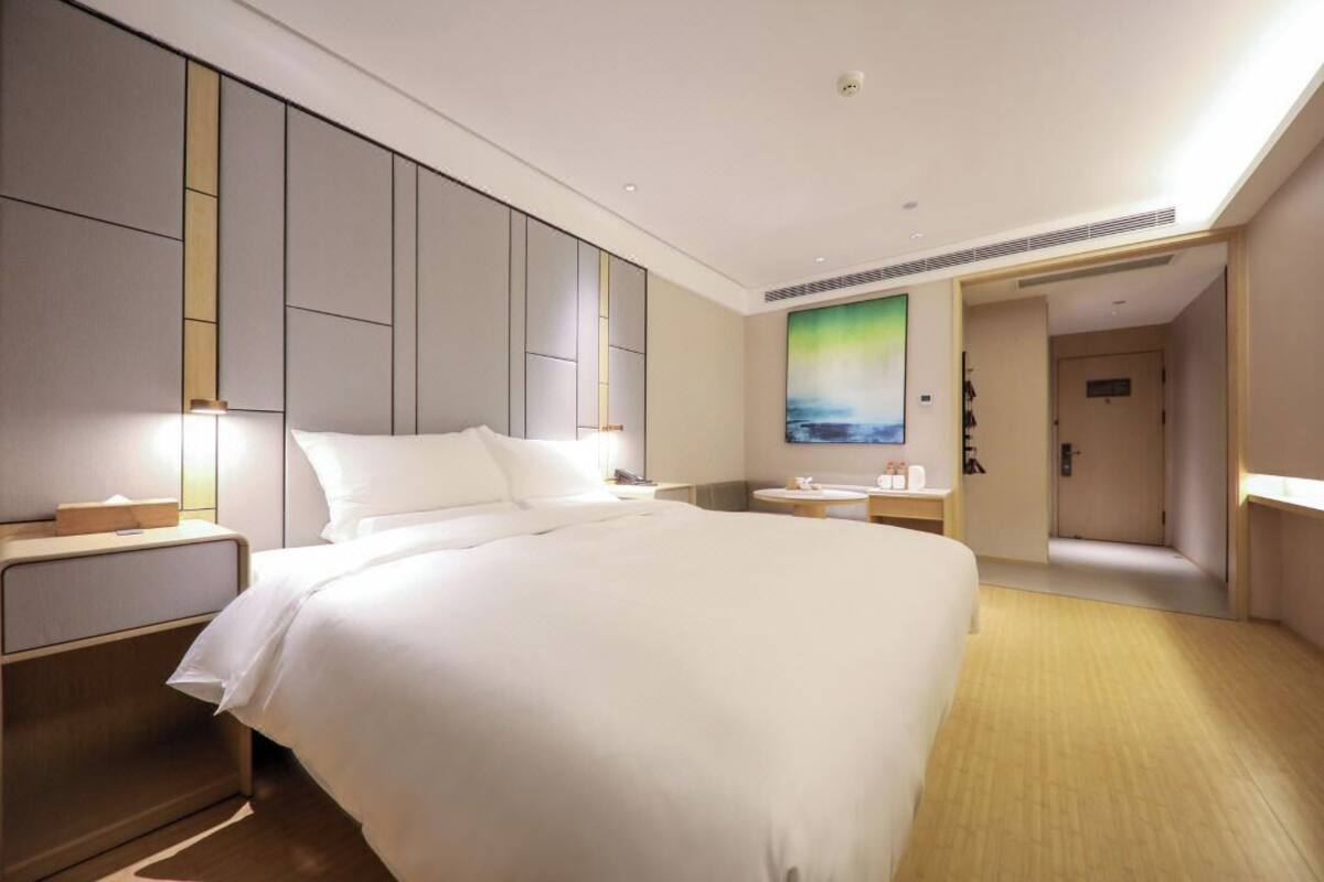 A modern hotel room with a large bed, bedside tables, a bathroom with a shower, and a painting on the wall.