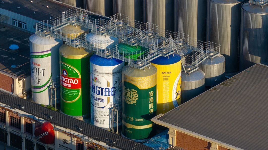 Grandes tanques industriales de almacenamiento con etiquetas, una escalera de metal y un edificio con techo plano.