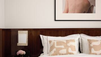 A bedroom with a bed, pillows, a bedside table, a mirror, and a framed picture on the wall.