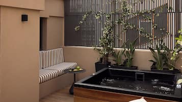 Un espace extérieur moderne, aménagé avec des sièges, un jacuzzi noir, des coussins à rayures et des plantes en pot.