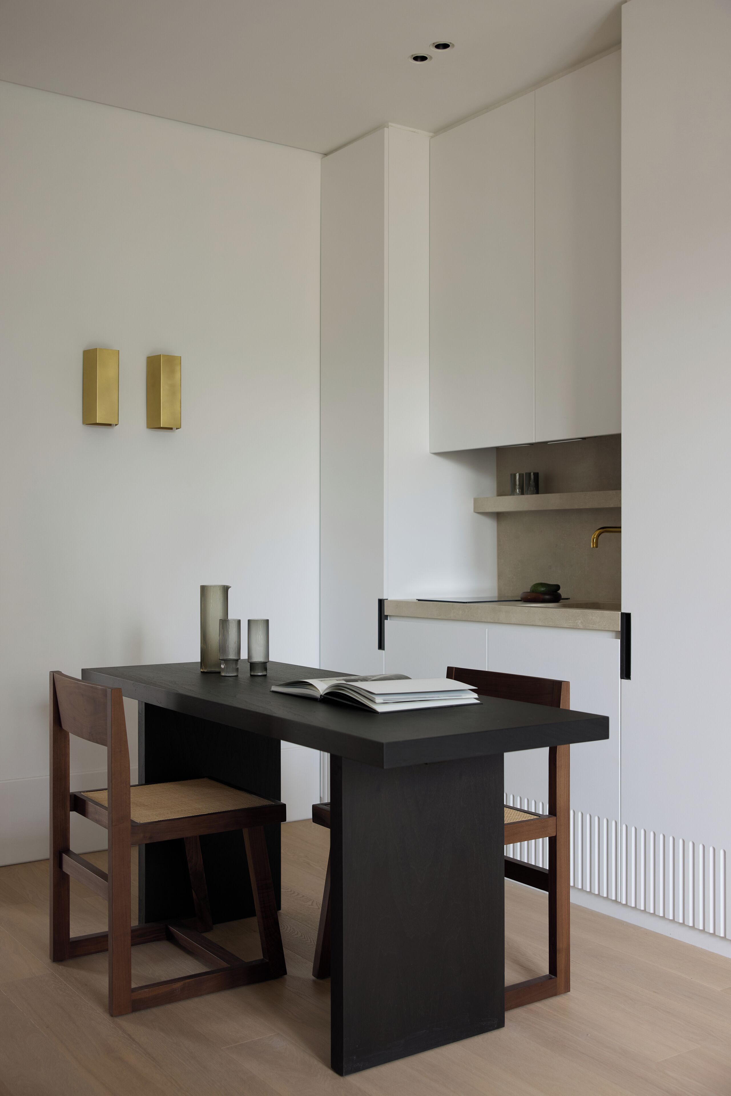A modern dining area with a dark table, two wooden chairs, and a book.