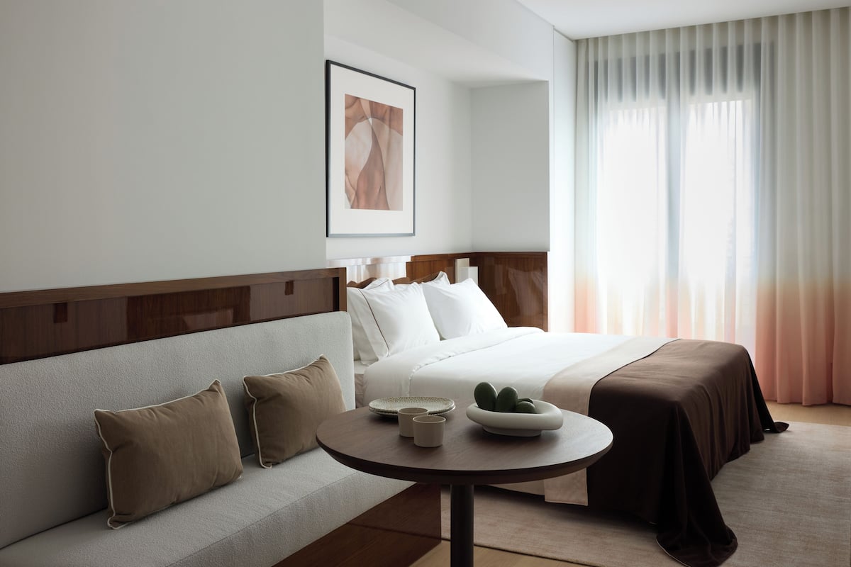 A hotel room with a bed, a sofa, a round table with a bowl of fruit, and a framed picture on the wall.