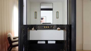 Un baño moderno con un espejo grande, un lavamanos blanco y una encimera de mármol negro. Hay dos luces empotradas en la pared y un perchero para toallas.