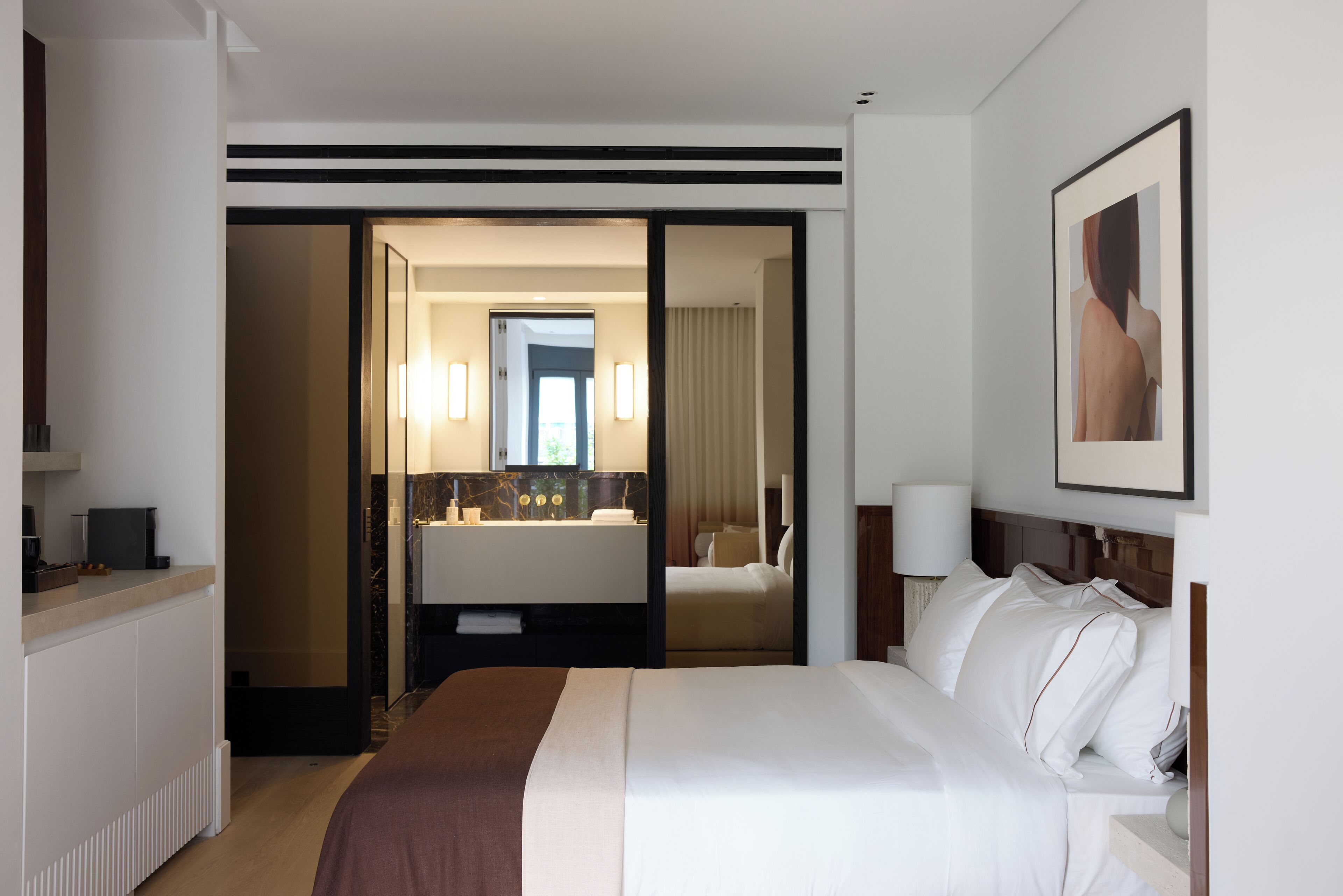 A hotel room with a large bed, a desk with a computer, a bathroom with a mirror, and a framed picture on the wall.