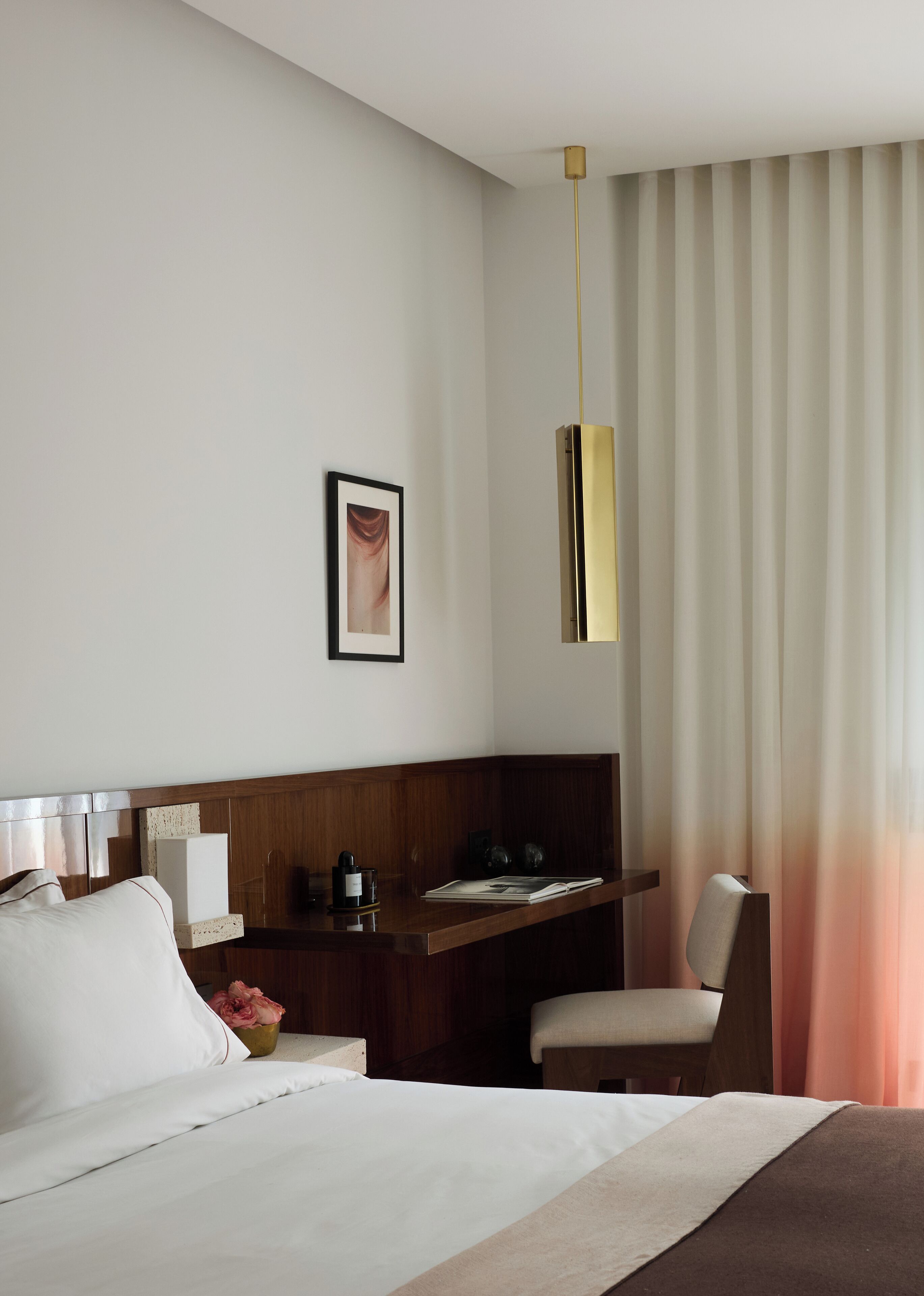 A hotel room with a bed, a desk, a chair, a picture on the wall, and a curtain.
