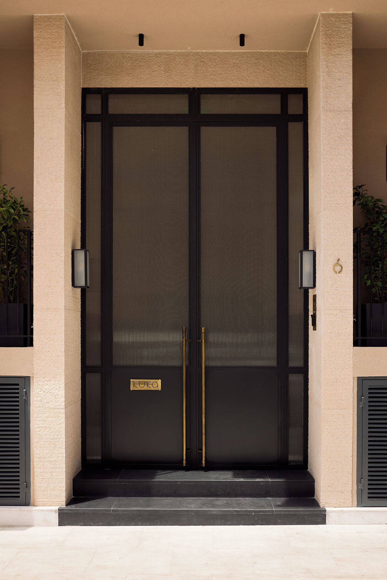 Une grande porte double, de couleur sombre, avec une enseigne portant l’inscription « KUKO » et deux poignées verticales.