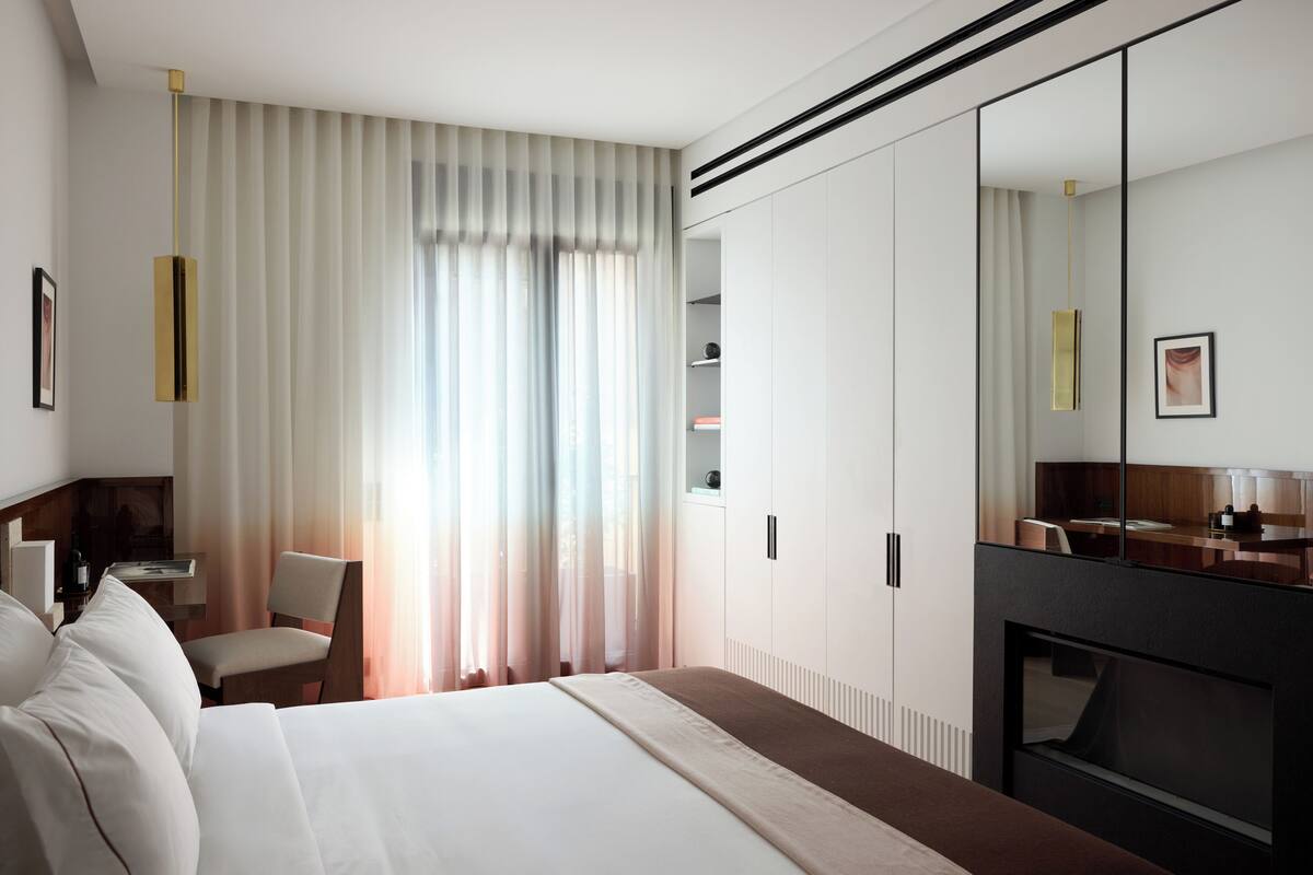 A modern hotel room with a large bed, a seating area with a chair, a desk, and a large mirror.