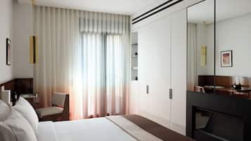 A modern hotel room with a large bed, a seating area with a chair, a desk, and a large mirror.