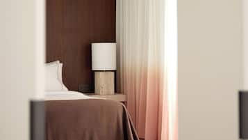 A hotel room with a bed, a nightstand, a lamp, and a window with curtains.