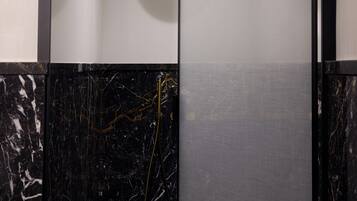 A modern bathroom with a black marble floor, a gold showerhead, and a glass partition.