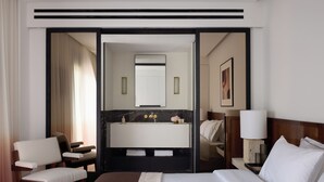 Une chambre d’hôtel dotée d’un grand lit, d’un coin salon avec des fauteuils, d’une coiffeuse avec un miroir et d’une table de chevet avec une lampe.