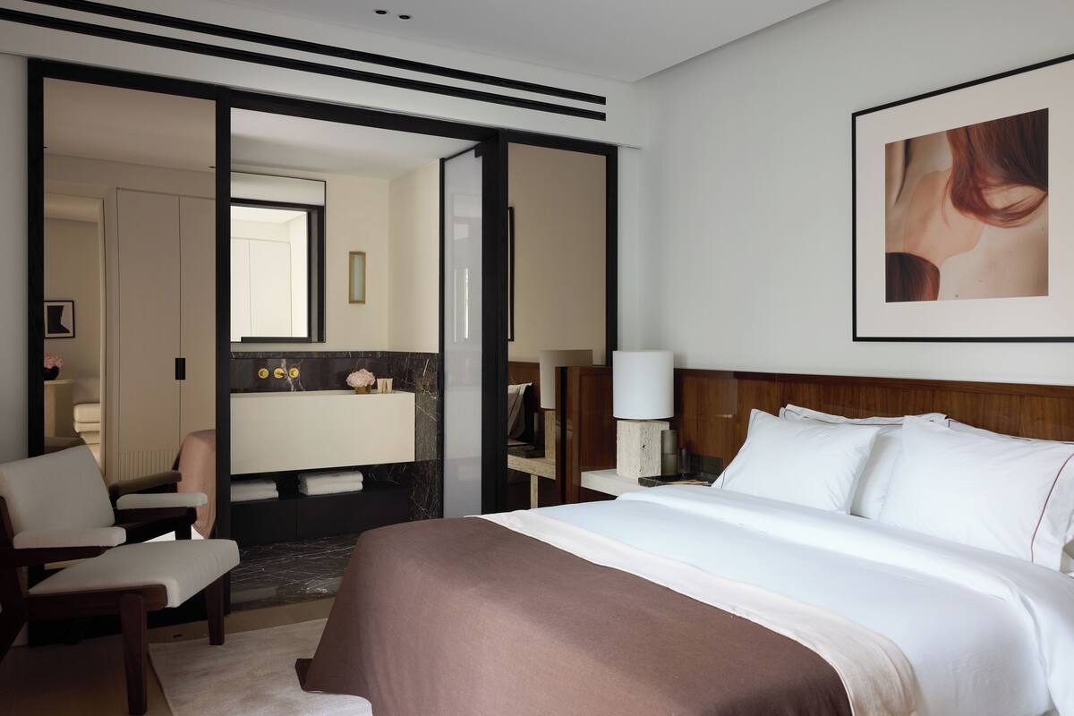 A hotel room with a large bed, a sitting area with a chair, a vanity with a mirror, and a framed picture on the wall.