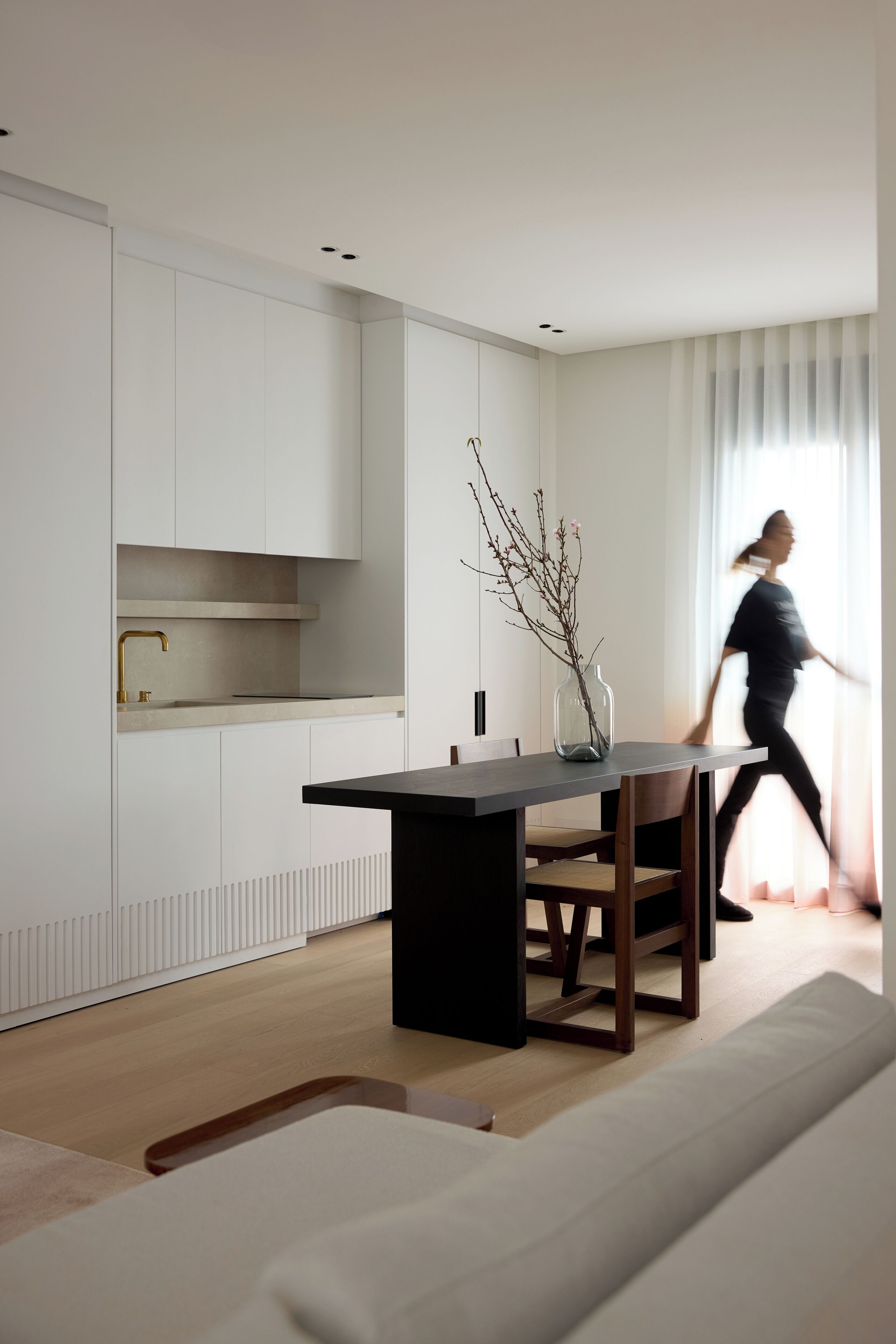 Una cocina moderna con armarios blancos, un comedor de mesa oscura y un jarrón con ramas.