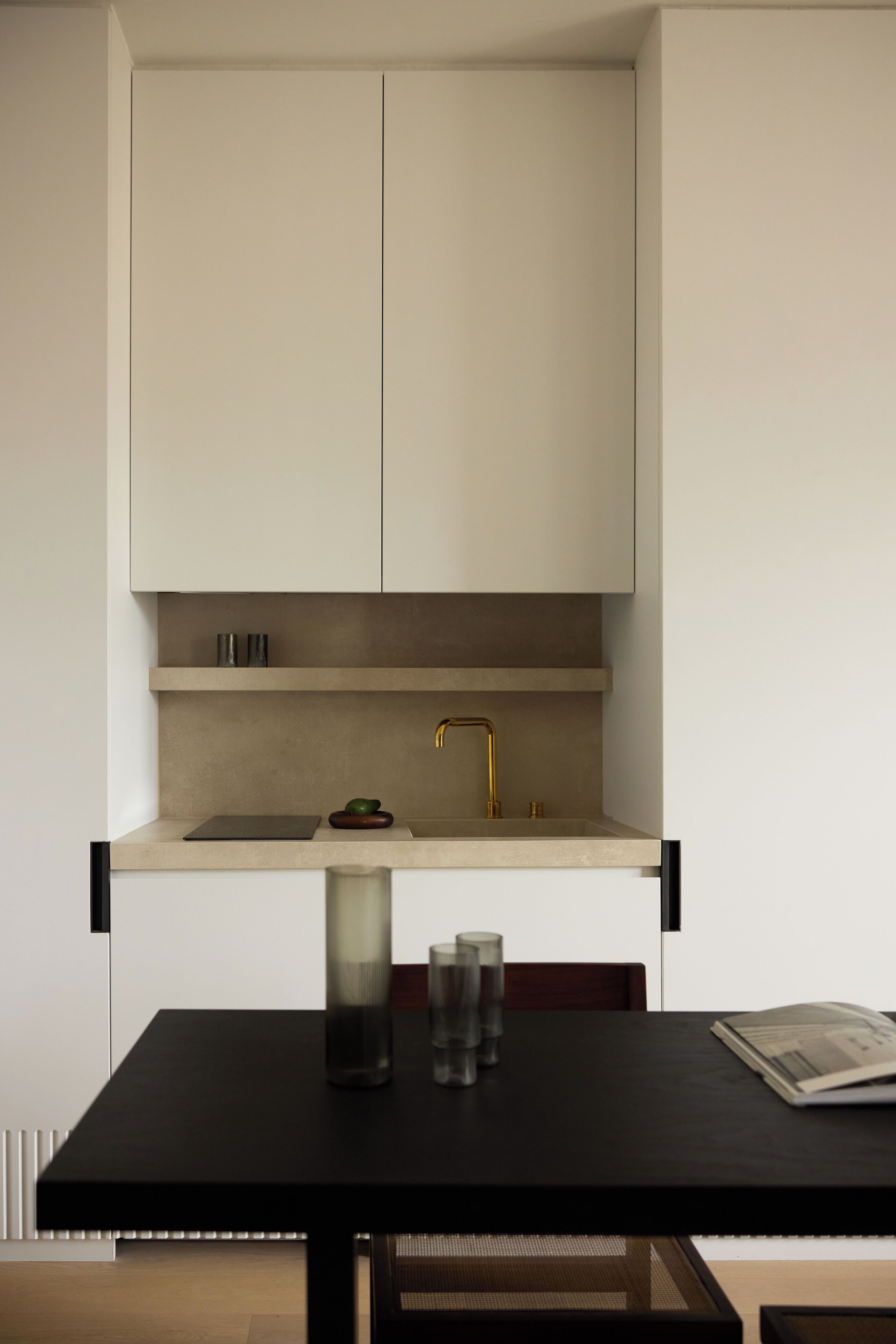 A modern kitchen with a minimalist design, featuring a black countertop, a single gold faucet, and a small shelf with two containers.
