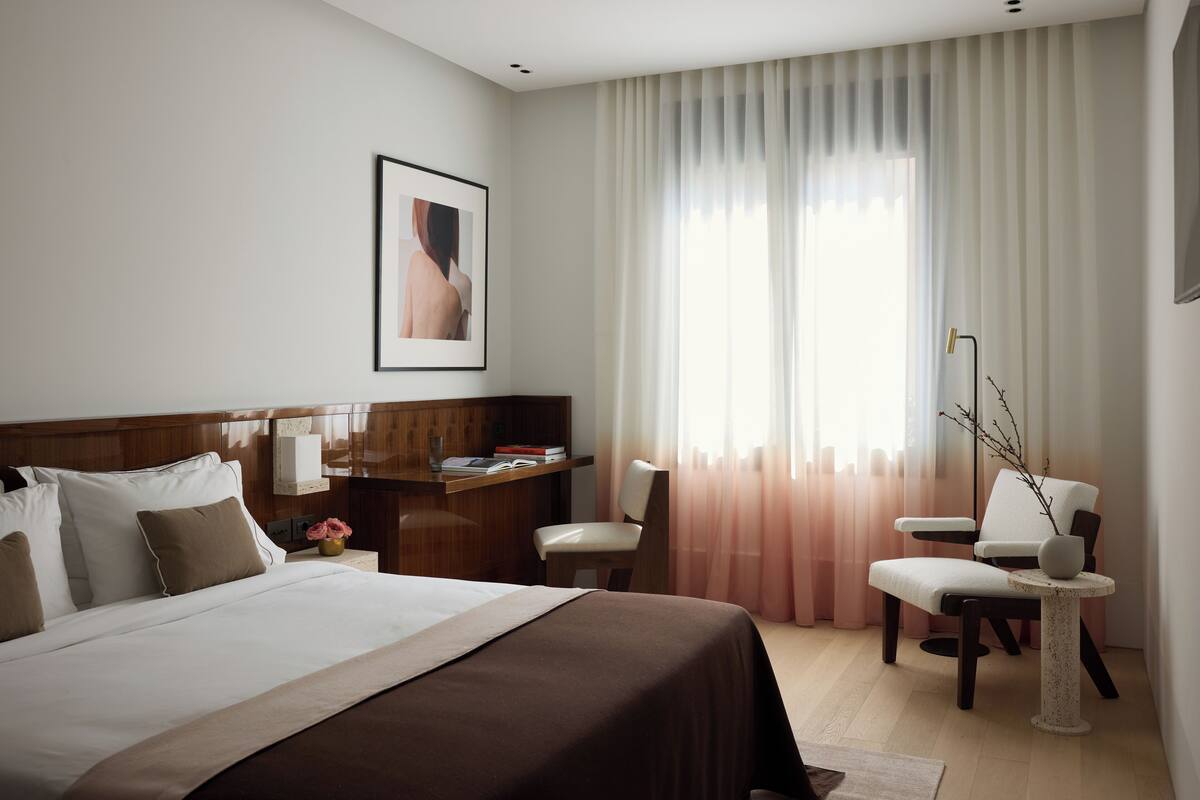 A hotel room with a large bed, a desk, a chair, and a small table.