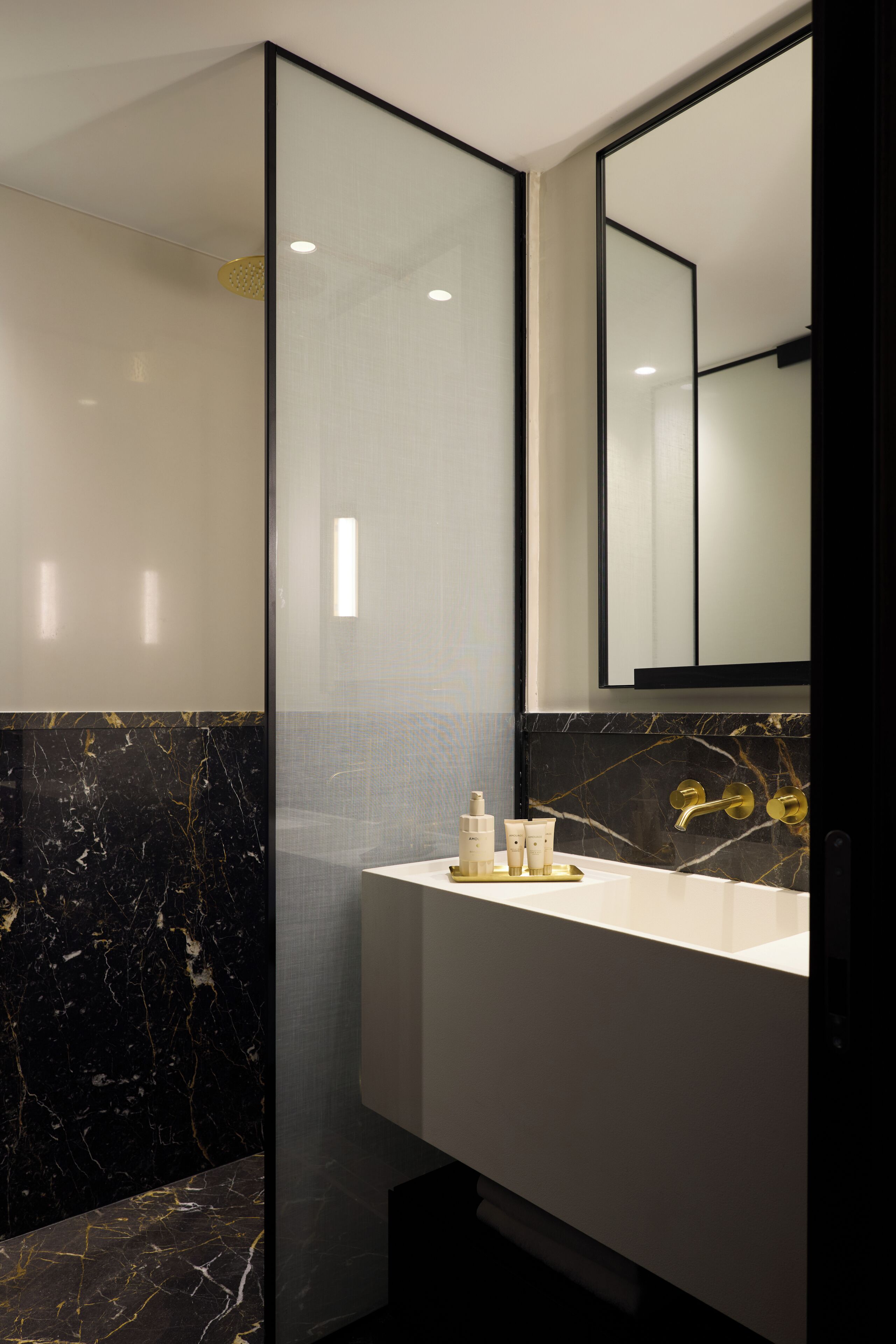A modern bathroom with a glass shower enclosure, a white sink with gold fixtures, and a marble-tiled wall.