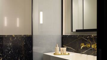 A modern bathroom with a glass shower enclosure, a white sink with gold fixtures, and a marble-tiled wall.