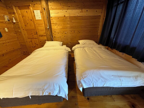 A cabin-style room with two single beds, wooden walls, and a window with curtains. - Hirafu Cottage (Kutchan)
