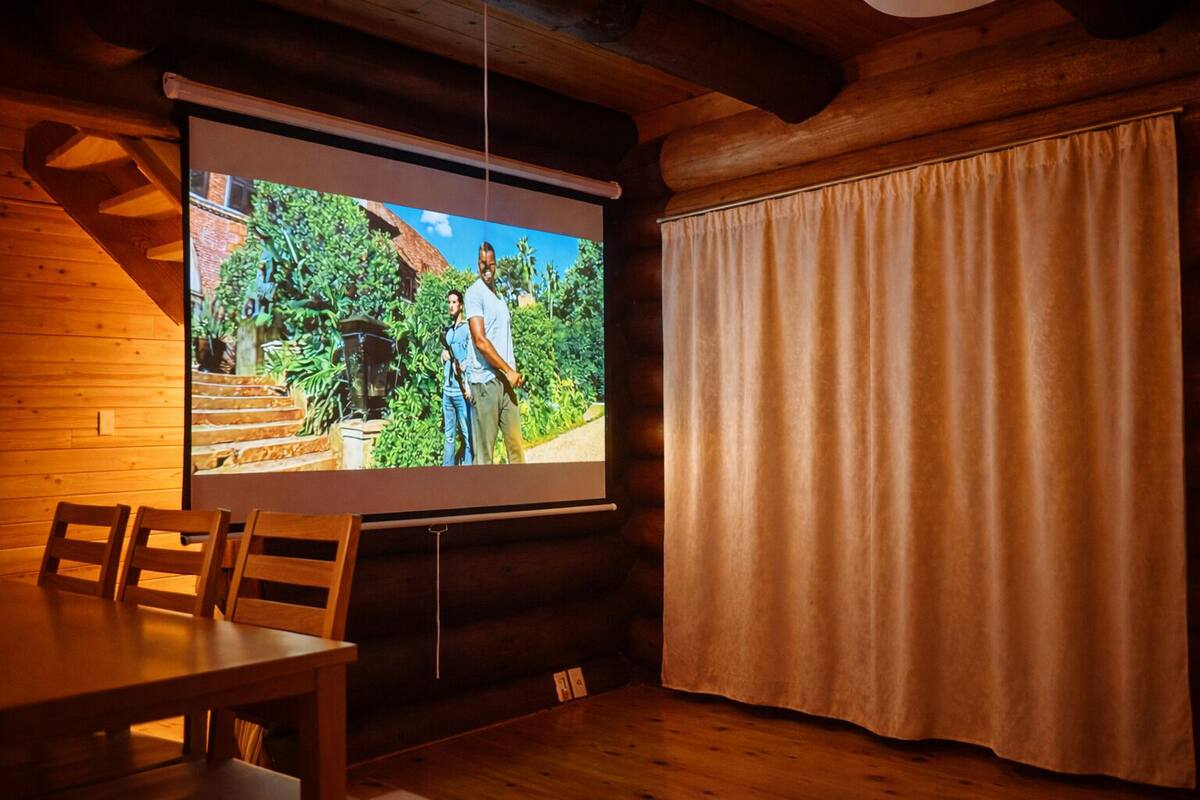 A room with a wooden interior, a projection screen, a table, and a curtain.