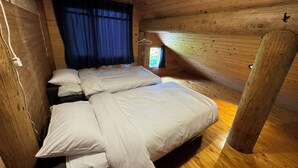 A cozy cabin room with a wooden interior, a bed with white bedding, and a window with curtains. - Hirafu Cottage (Kutchan)