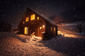 A wooden cabin with a snow-covered roof, a lit entrance, and a snow-covered ground. - Hirafu Cottage (Kutchan)
