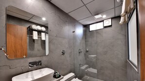 A modern bathroom with a large mirror, a white sink, a toilet, and a shower area. - Soil to Soul Trinity Hotel - A Boutique Stay (Veraval)