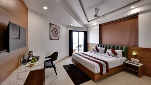 A modern hotel room with a large bed, a desk with a chair, a television, and a window with curtains. - Soil to Soul Trinity Hotel - A Boutique Stay (Veraval)