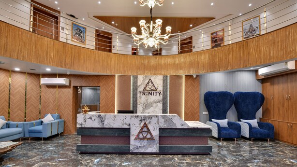 A lobby with a reception desk, blue seating, a chandelier, and a wooden wall design. - Soil to Soul Trinity Hotel - A Boutique Stay (Veraval)