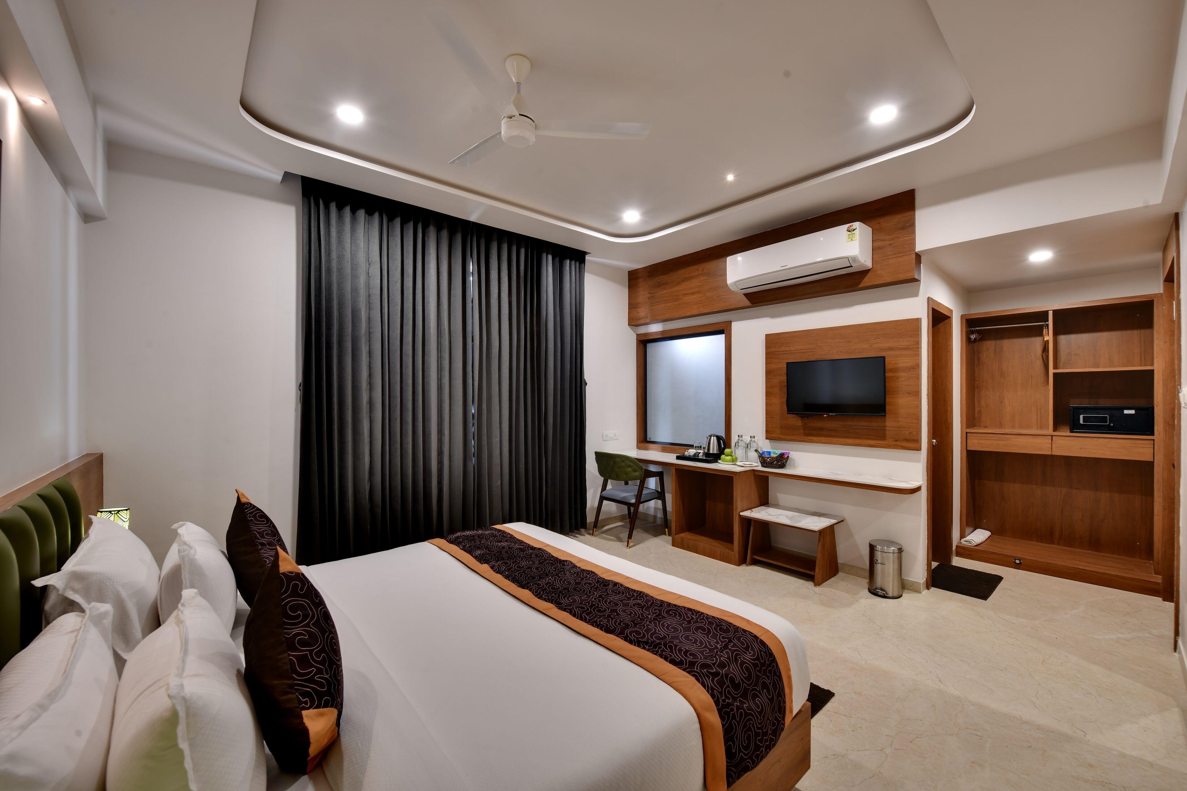 A modern hotel room with a large bed, a desk, a chair, a TV, and built-in wardrobes.
