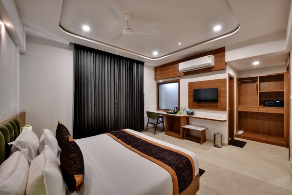 A modern hotel room with a large bed, a desk, a chair, a TV, and built-in wardrobes. - Soil to Soul Trinity Hotel - A Boutique Stay (Veraval)