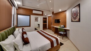 A hotel room with a bed, desk, chair, TV, and artwork. - Soil to Soul Trinity Hotel - A Boutique Stay (Veraval)