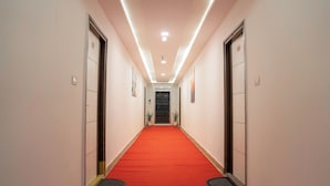 A hallway with a red carpet, white walls, and doors on both sides. - Hotel Euphoria Urban Sleep (Hyderabad)