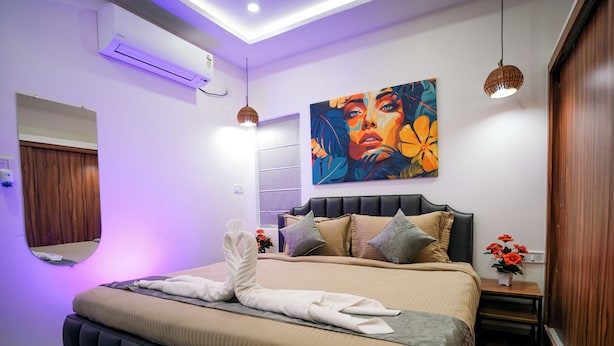 A modern bedroom with a large bed, a wall-mounted air conditioner, a painting, and a small table with flowers. - Hotel Euphoria Urban Sleep (Hyderabad)