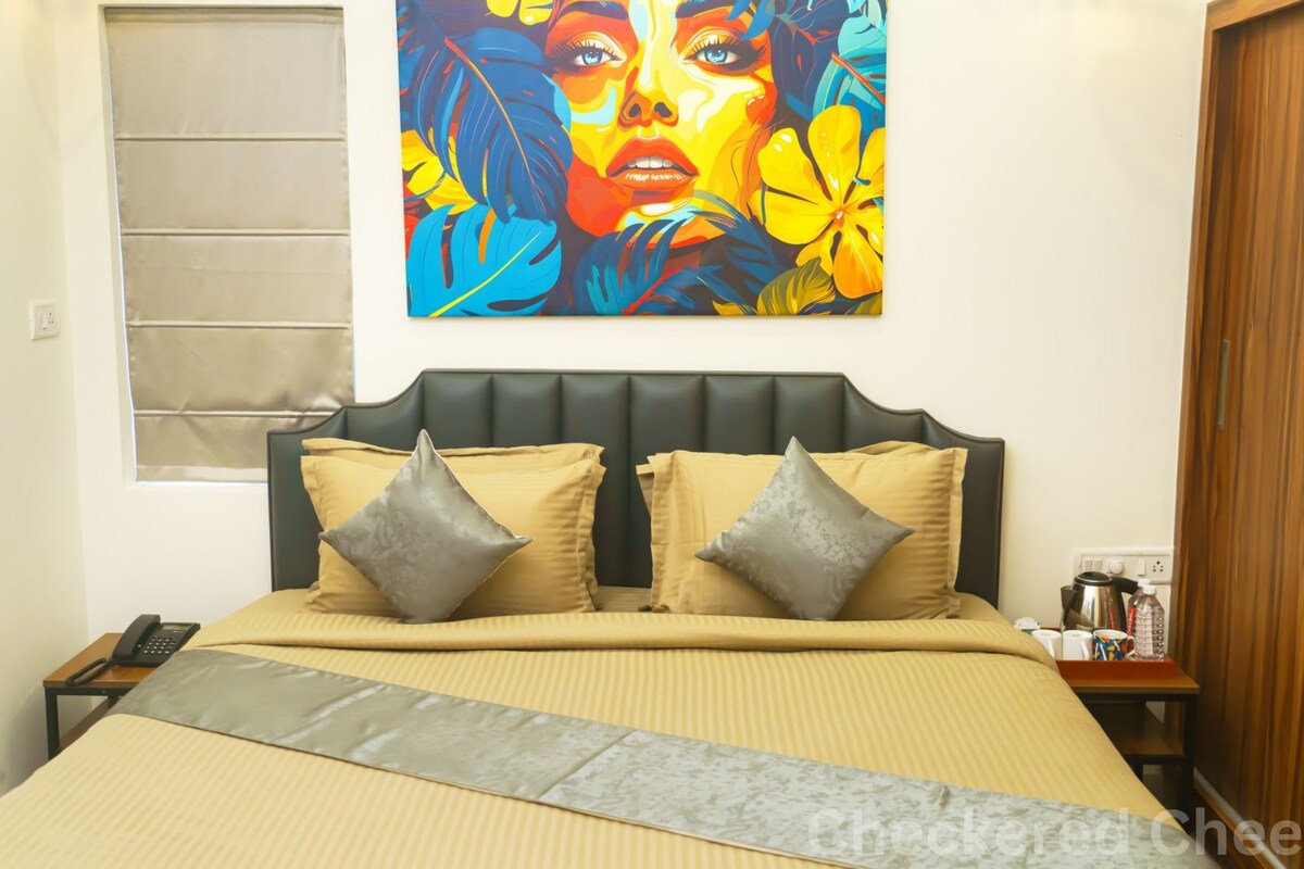 Quarto com uma cama, duas almofadas, mesa de cabeceira com telefone, um criado-mudo e um quadro pendurado na parede.