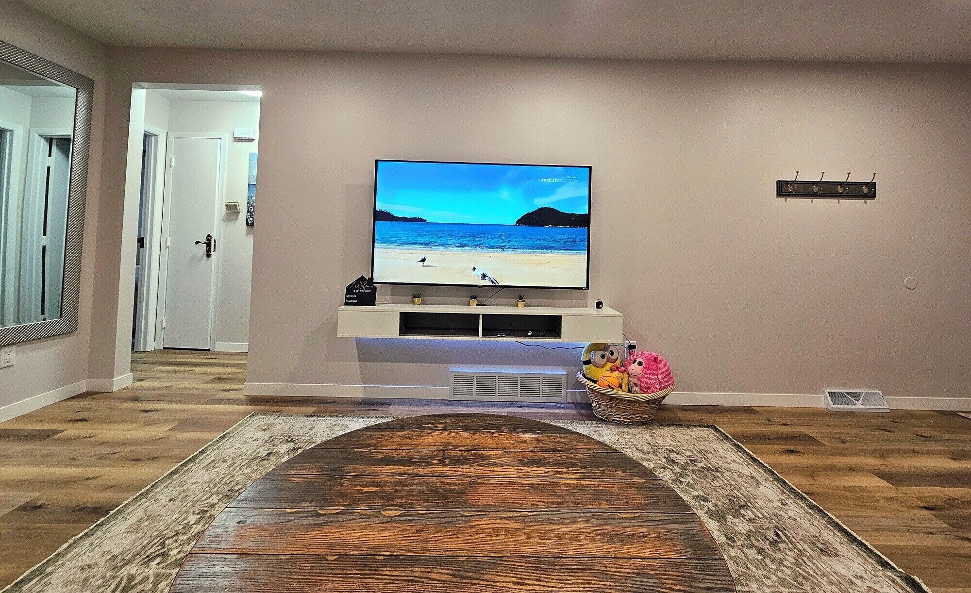 Un salon avec un téléviseur à écran plat fixé au mur, un plancher en bois et un tapis.