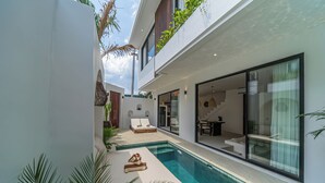 A modern residential building with a swimming pool, outdoor seating, and large windows. - Nova Oasis 1 (Canggu)