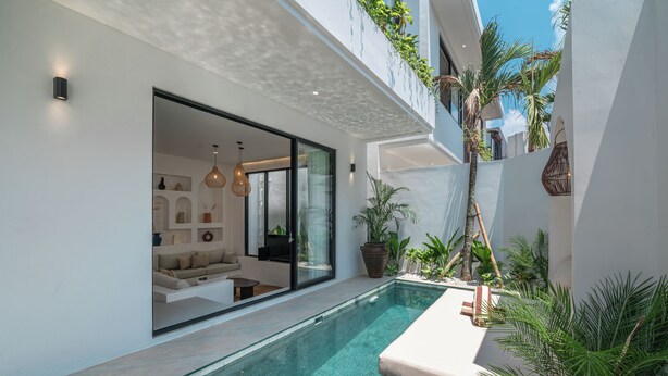A modern pool area with clear water, a built-in seating area, and lush greenery. - Nova Oasis 1 (Canggu)