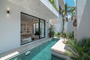 A modern pool area with clear water, a built-in seating area, and lush greenery. - Nova Oasis 1 (Canggu)