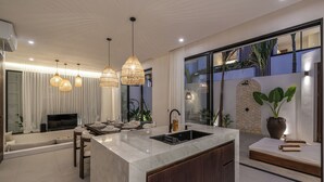A modern kitchen with a marble countertop, wooden cabinets, and pendant lighting. - Nova Oasis 1 (Canggu)